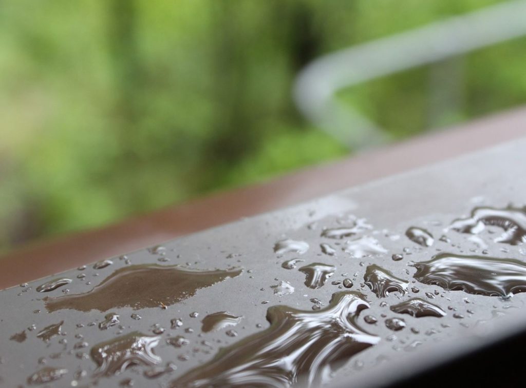 Water drops on a windowsill. Blurred greenery in the background. 